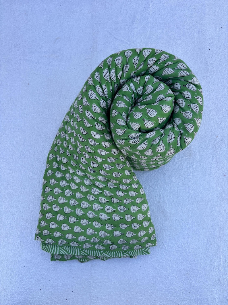 May include: A green cotton fabric with a white floral print. The fabric is rolled up into a spiral shape.