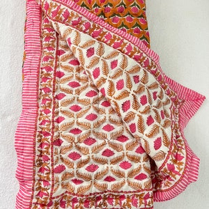 May include: A white cotton quilt with a pink and orange floral print. The quilt is folded in half and has a pink and white striped border.