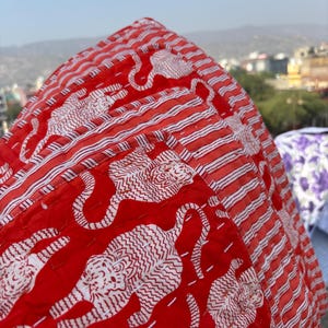 May include: Red and white kantha quilt with a striped border and a pattern of white tigers on a red background.