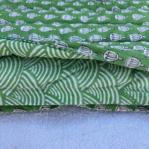 May include: Two pieces of green fabric with white printed designs. The top piece has a repeating pattern of white lotus flowers. The bottom piece has a repeating pattern of white curved lines.