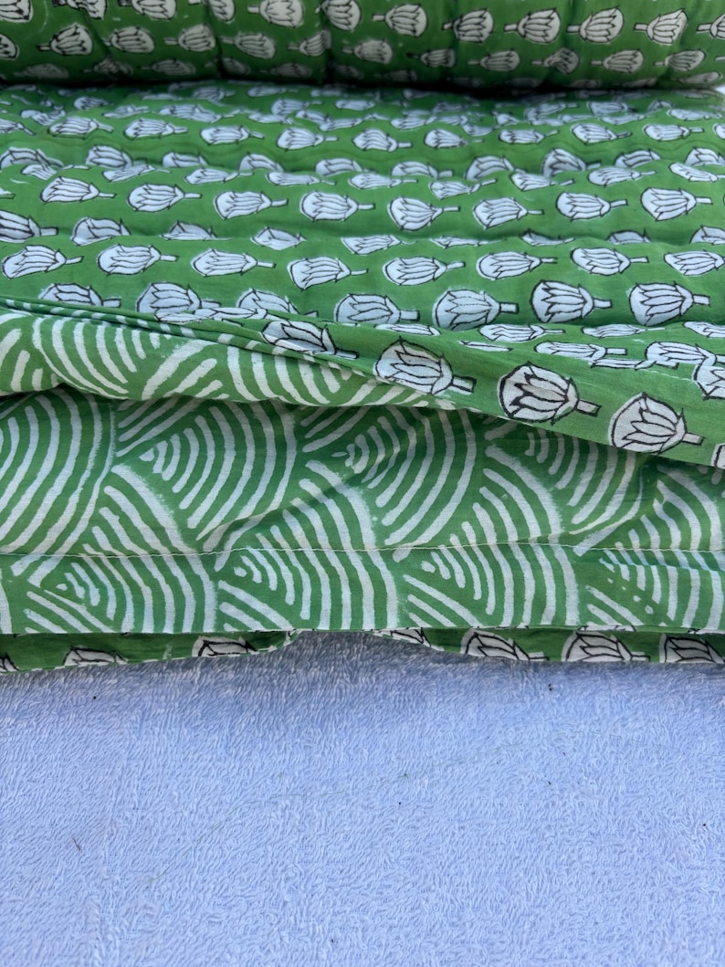 May include: Two pieces of green fabric with white printed designs. The top piece has a repeating pattern of white lotus flowers. The bottom piece has a repeating pattern of white curved lines.