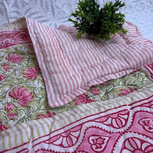 May include: A quilted textile set featuring a floral patterned base in shades of pink and green, with a striped pillow in pink and white. A small green plant sits atop the set. The set is designed for comfort and style.