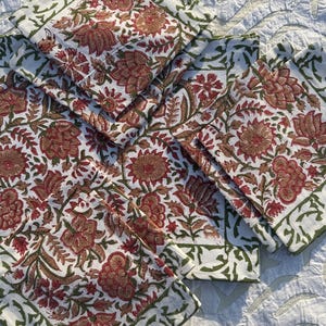 Op de afbeelding: Set van zes witte katoenen servetten met een groene en rode bloemenprint. De servetten hebben een groene rand met een bloemenontwerp.