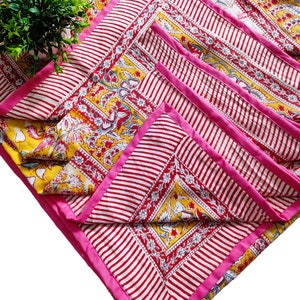 May include: A set of four pink and white striped placemats with a yellow floral pattern and pink trim. The placemats are folded and stacked on top of each other.