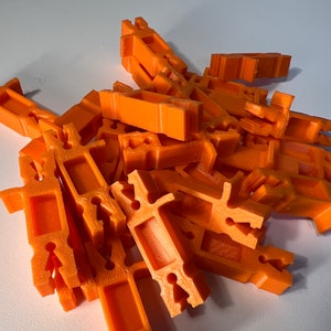 May include: A pile of orange plastic 3D printed connectors. The connectors have a variety of shapes and sizes.