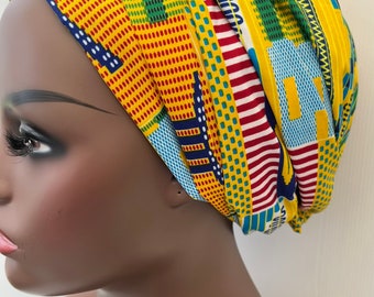 Puede incluir: Un turbante para la cabeza con estampado amarillo, azul, rojo y verde. El turbante está anudado en la parte superior de la cabeza.