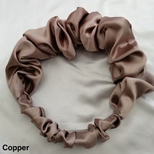 May include: A copper-colored satin hair scrunchie, made of soft, smooth fabric. The scrunchie is gathered into a circle shape, creating a ruffled look.