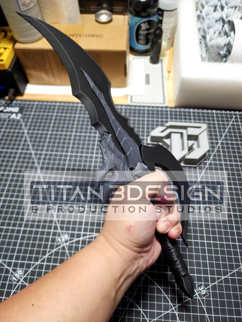 K&ouml;nnte beinhalten: Ein schwarzes und graues Dolch mit einer strukturierten Klinge und einem schwarzen Griff. Der Dolch wird von einer Hand gehalten. Der Text "TITAN3DESIGN & PRODUCTION STUDIOS" ist im Bild sichtbar.