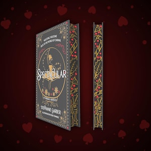 May include: A black hardback book with a gold and red design. The book title is "SPECTACULAR" and the author is Stephanie Garber. The book is a carnival novella.
