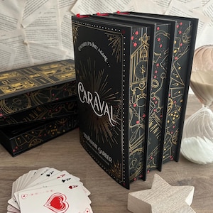 Può includere: Un set di tre libri in brossura rigida neri con dettagli dorati e rossi. La copertina del libro a destra presenta il titolo "Caraval" in lettere dorate su uno sfondo nero e dorato. Il testo "Remember it's only a game..." è stampato in bianco sulla copertina. Il nome dell'autore, "Stephanie Garber", è stampato in lettere dorate sulla copertina.