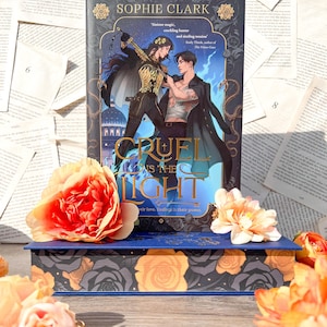 May include: A blue hardcover book with a gold and black floral design. The book title is "Cruel Prince is the Light" and the author is Sophie Clark. The book cover features two people in a fantasy setting.