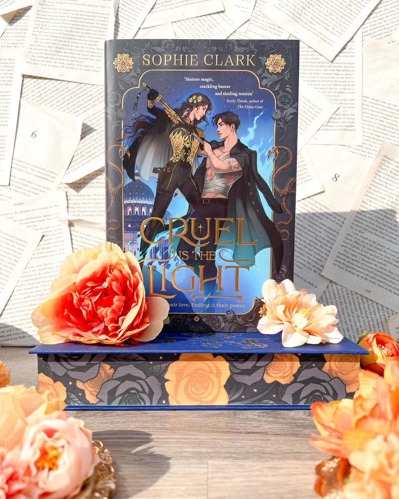 May include: A blue hardcover book with a gold and black floral design. The book title is "Cruel Prince is the Light" and the author is Sophie Clark. The book cover features two people in a fantasy setting.