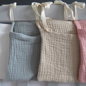 May include: Four fabric storage pockets hanging on a white rod. The pockets are white, gray, beige, and pink.