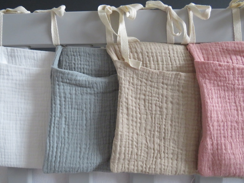 May include: Four fabric storage pockets hanging on a white rod. The pockets are white, gray, beige, and pink.