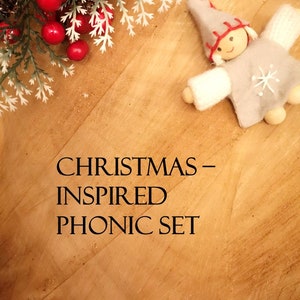 May include: A Christmas-inspired phonics set with a felt elf doll on a wooden background. The elf is wearing a gray hat and white mittens. The text "CHRISTMAS - INSPIRED PHONIC SET" is printed on the wood.