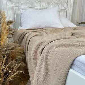 Pu&ograve; includere: Una coperta beige a nido d'ape &egrave; drappeggiata su un letto bianco con un cuscino bianco. La coperta &egrave; realizzata in tessuto morbido e traspirante, perfetta per aggiungere un tocco di calore e stile a qualsiasi camera da letto.