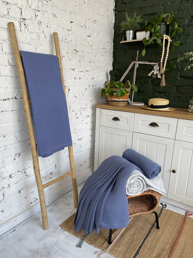May include: Two blue waffle weave blankets, one folded and placed on a wooden ladder, the other folded and placed on a wicker stool with a white blanket underneath. The stool is on a woven rug with black and white stripes.