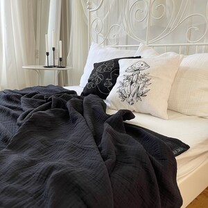 Pu&ograve; includere: Una coperta nera a nido d'ape drappeggiata su un letto bianco con baldacchino bianco e due cuscini decorativi. Un cuscino presenta un disegno a linea nera e bianca di un viso e l'altro cuscino presenta un disegno a linea nera e bianca di un fungo e cristalli.