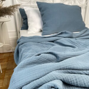May include: A blue waffle weave throw blanket is folded on a bed with white pillows. The blanket is made of a soft, textured fabric.