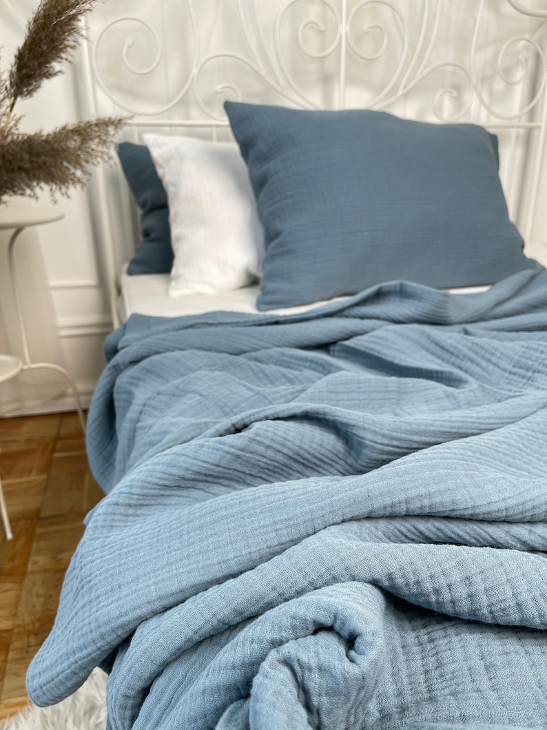 May include: A blue waffle weave throw blanket is folded on a bed with white pillows. The blanket is made of a soft, textured fabric.