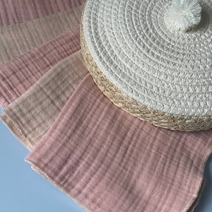 May include: A set of four pink and beige muslin cloths with a white woven round lid with a pom pom on top.
