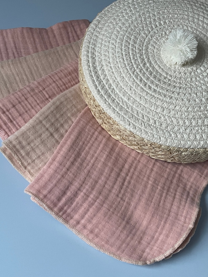 May include: A set of four pink and beige muslin cloths with a white woven round lid with a pom pom on top.