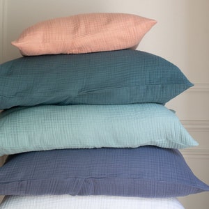 May include: A stack of five pillows in various shades of blue, green, and pink. The pillows are made of a soft, textured fabric and are arranged in a pyramid shape.