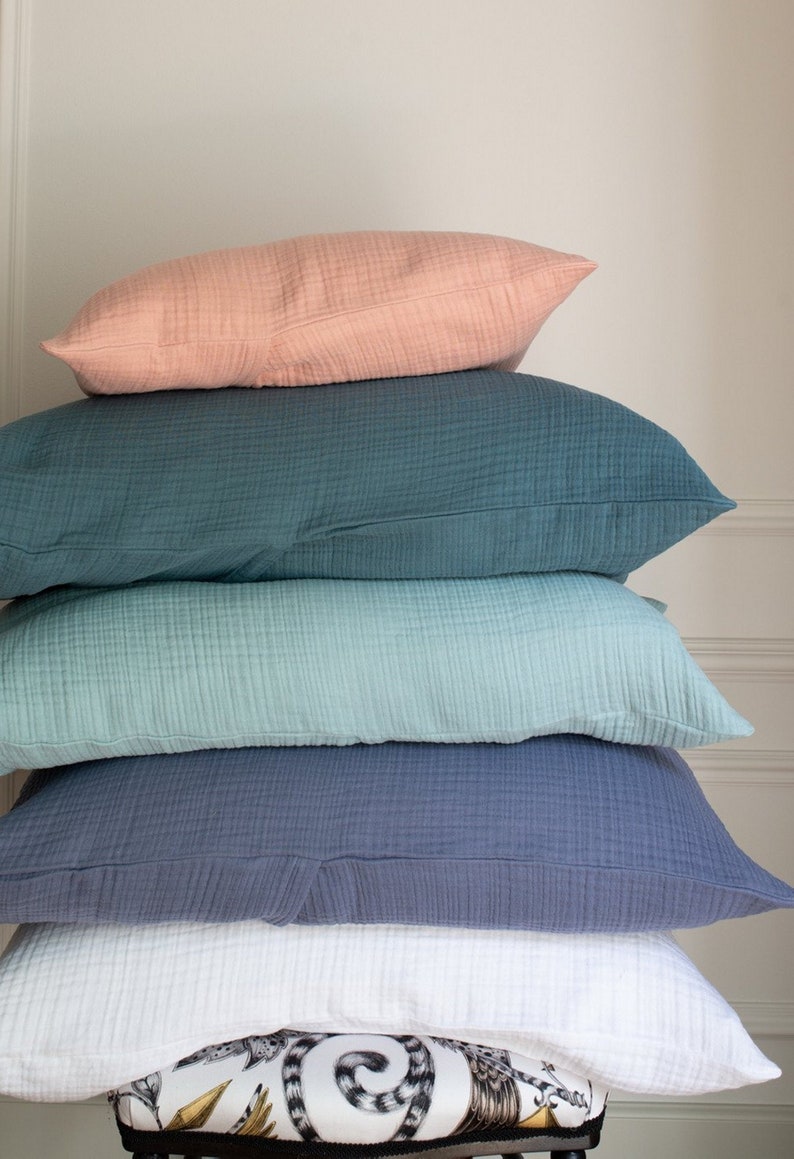 May include: A stack of five pillows in various shades of blue, green, and pink. The pillows are made of a soft, textured fabric and are arranged in a pyramid shape.