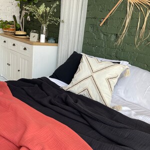 Pu&ograve; includere: Una coperta getta in nero e corallo con un cuscino bianco con un motivo geometrico su un letto con lenzuola bianche.