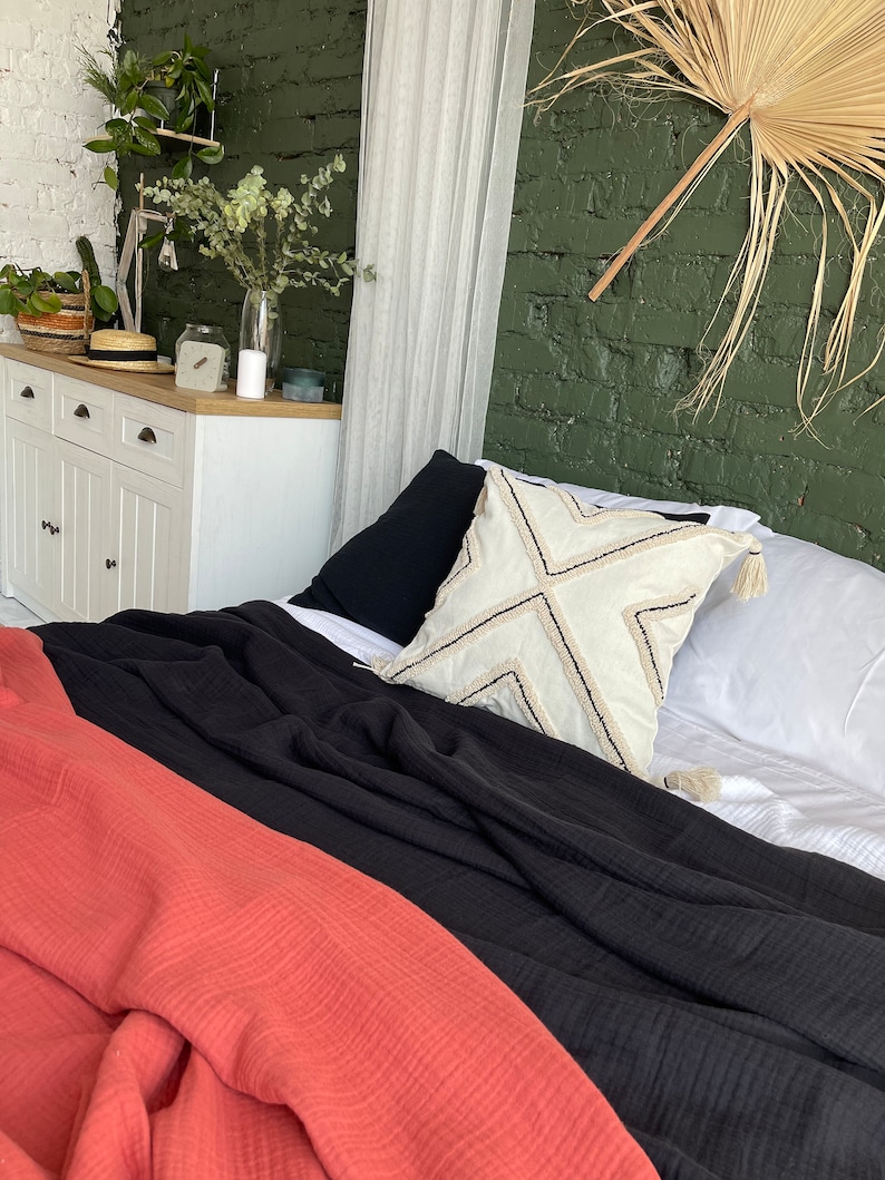 Pu&ograve; includere: Una coperta getta in nero e corallo con un cuscino bianco con un motivo geometrico su un letto con lenzuola bianche.