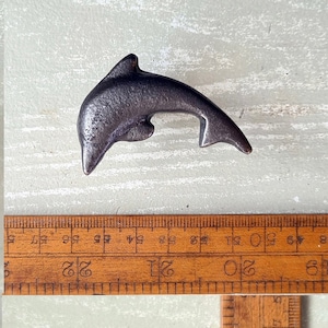 May include: A silver-colored metal dolphin figurine. The dolphin is about 2 inches long and is in a jumping pose.