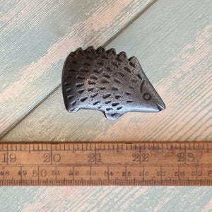 May include: A silver metal hedgehog figurine with a textured surface. The figurine is approximately 5 cm long.
