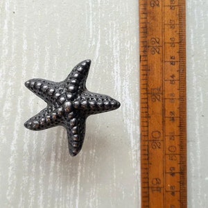 May include: A silver metal starfish with a textured surface. The starfish is approximately 5 cm in diameter.