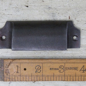 May include: A dark gray metal drawer pull with rounded edges and two screw holes. The pull is approximately 3 inches long.