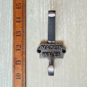 Pode incluir: Um gancho de casaco de metal prateado com uma placa retangular que diz "MADE IN WALES".