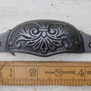 May include: A cast iron drawer pull with a decorative floral design. The pull is approximately 3 inches long and has a black finish.