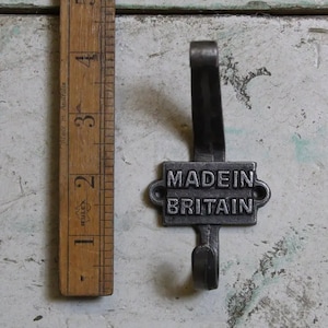 Pode incluir: Um gancho de metal preto com uma placa retangular que diz "MADE IN BRITAIN".