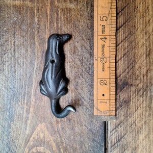 Pode incluir: Gancho de metal preto em forma de cão com cauda enroscada. O gancho tem aproximadamente 10 cm de altura.