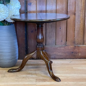 May include: A dark brown wooden table with a round top and three legs. The table is made of wood and has a simple design.