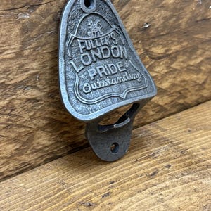 Op de afbeelding: Een zilveren metalen flessenopener met een reliëfdesign met de tekst "Fuller's London Pride Outstanding".