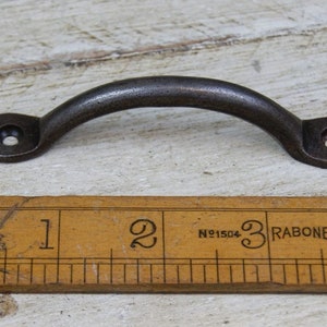 Könnte beinhalten: Ein schwarzer Metall-Schubladenzug mit einem gebogenen Griff und zwei runden Löchern. Der Zug ist etwa 7,6 cm lang.