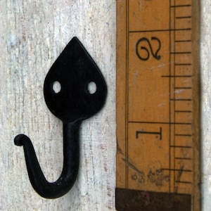 Pode incluir: Gancho de metal preto com uma parte superior pontiaguda e um gancho curvo. O gancho mede aproximadamente 5 cm de comprimento e é mostrado ao lado de uma régua.