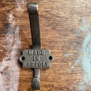 Pode incluir: Um gancho de metal preto com uma placa retangular que diz "MADE IN NORFOLK".