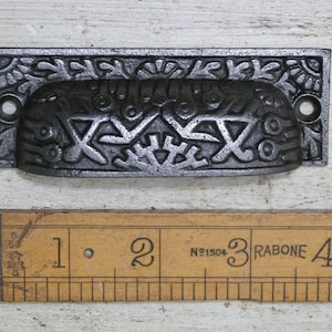 Op de afbeelding: Een zwarte gietijzeren ladetrekker met een sierlijk ontwerp. De trekker is ongeveer 7,6 cm lang.