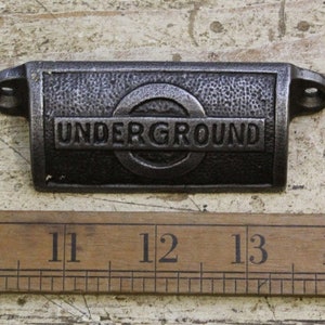 May include: A cast iron drawer pull with a black finish. The pull features the London Underground logo and the word "UNDERGROUND".