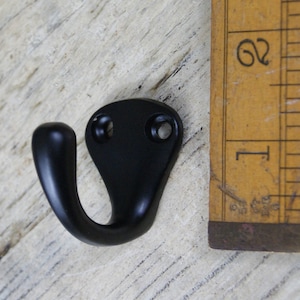 Pode incluir: Gancho de metal preto com dois furos para parafusos. O gancho mede aproximadamente 5 cm de comprimento e tem uma forma arredondada.