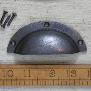 May include: A dark gray, semi-circular cabinet pull with three screw holes and three black screws. The pull is approximately 5 inches wide. The hardware has a rustic, industrial aesthetic.