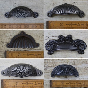Peut inclure: Six styles différents de poignées de tiroir en fonte noire. Les poignées mesurent environ 10 cm de long et présentent une variété de motifs, notamment une coquille, un motif floral et un motif enroulé.