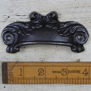 May include: Black cast iron drawer pull with a decorative floral design. The pull measures approximately 3 inches in length.