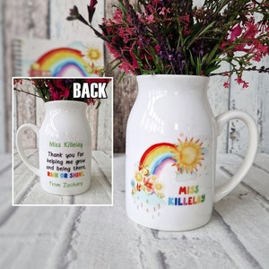 May include: White ceramic mug with a rainbow, sun, and flowers design. The mug says "Miss Killelay" and has the text "Thank you for helping me grow and being there. Rain or Shine. From Zachary" on the back.